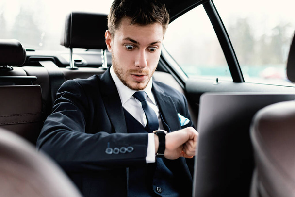Nuori liikemies katselee rannekelloa autossaan - Valokuva, kuva