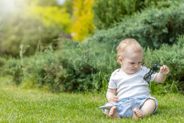 Little boy is viewing his sunglasses sitting in the garden - Φωτογραφία, εικόνα