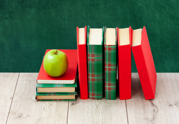 Back to school, pile of books in colorful covers and green apple on wooden table with empty green school board background. Distance home education. Quarantine concept of stay home - Фото, зображення