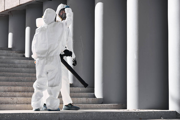 Дезинфекция города. профессиональный работник в защитном костюме очищает лестницу - Фото, изображение