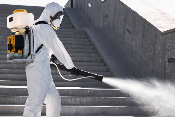 disinfector in protective antiviral suit, chemical decontamination sprayer bottle outdoors - Фото, зображення