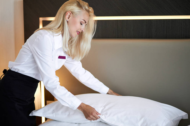 chambermaid tidies the bed in hotel room - Fotoğraf, Görsel