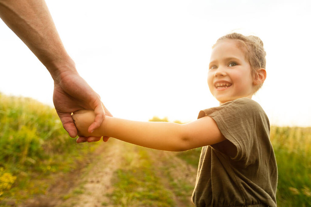 Kleines Mädchen hält die Hand ihres Vaters und blickt zurück - Foto, Bild