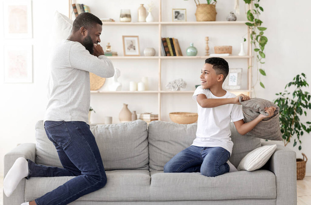 Ευτυχισμένες στιγμές μαζί. Μαύρος μπαμπάς μαξιλαροπόλεμος με τον γιο Preteen στο σπίτι - Φωτογραφία, εικόνα