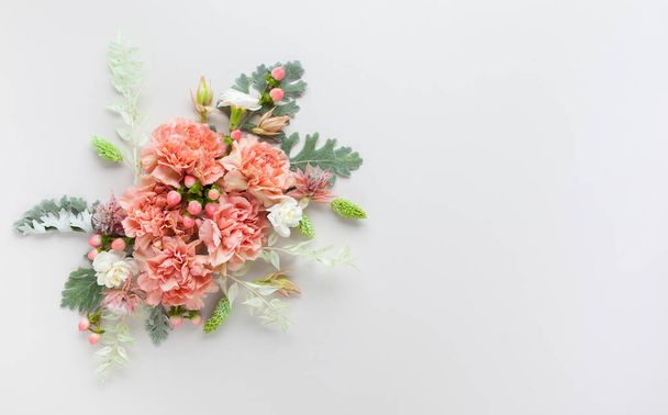 Flowers composition made of coral carnation and silver-green leaves of Senecio cineraria on pastel grey background. Nature concept, copy space, flat lay. - Photo, image