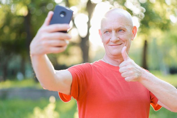 Positive senior man communicating online, showing thumb up gesture in the park - Photo, Image