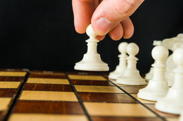 The part of a mans hand that makes the first move in a chess game, raising and moving a pawn one square forward. Dark background. - Photo, Image