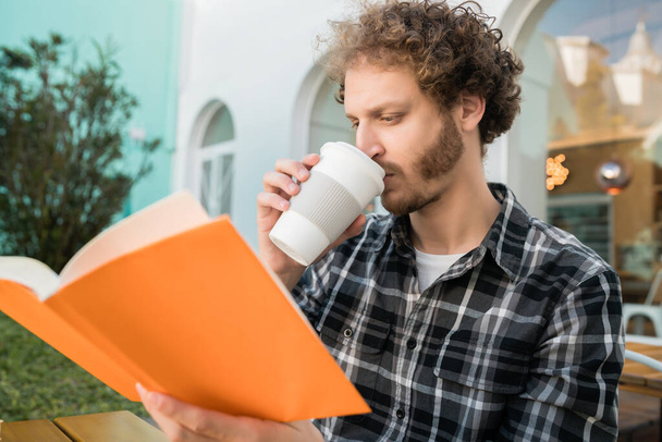 Retrato de homem caucasiano desfrutando de tempo livre e lendo um livro enquanto sentado ao ar livre no café. - Foto, Imagem