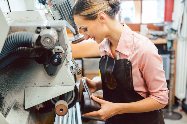 Vrouw schoenmaker werkt aan machine in haar schoenmaker workshop - Foto, afbeelding