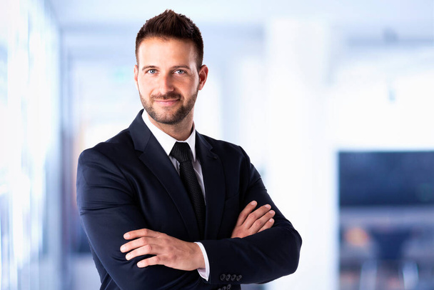 Portrait shot of arms crossed handsome businessman wearing suit while standing in the office.  - Foto, Imagen