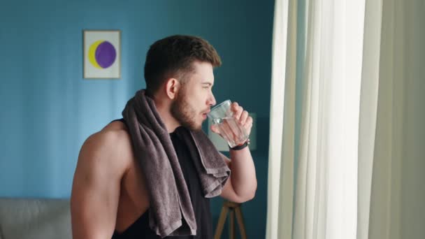 Starker Mann steht im Wohnzimmer und trinkt Wasser - Filmmaterial, Video