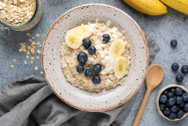 Healthy breakfast porridge oatmeal with banana, blueberry, coconut. Top view, concrete background - Foto, Imagen