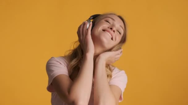 Beautiful cheerful blond girl happily listening music in headphones over colorful background. Good music - Imágenes, Vídeo