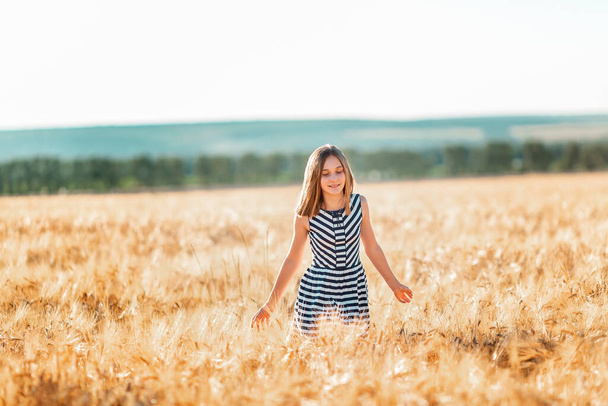 Happy teenage beautiful girl running down golden wheat field at the sunset - Zdjęcie, obraz