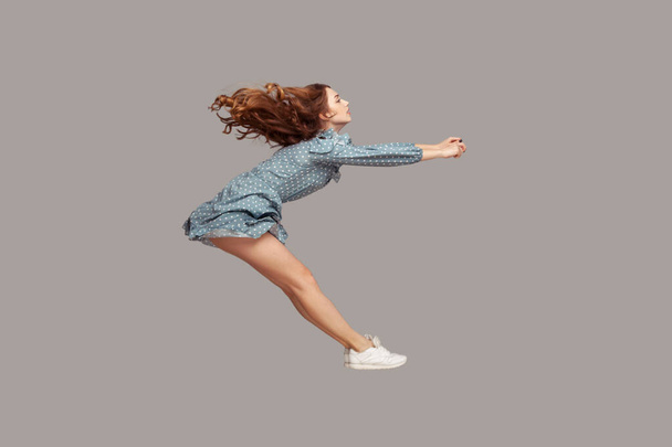 Side view girl rushing at full speed accelerate, steering driving fast and levitating in air. Model flying rapidly with hurricane wind blowing extremely sharply. indoor studio shot isolated on gray - Φωτογραφία, εικόνα