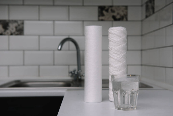 Water filters. Carbon cartridges and a glass on a white kitchen background. Household filtration system. - Foto, afbeelding