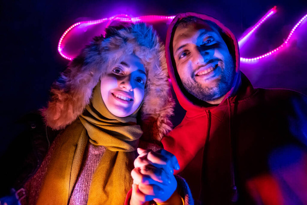 Happy arabic muslim siblings with colored lights behind them in dark room - Photo, Image