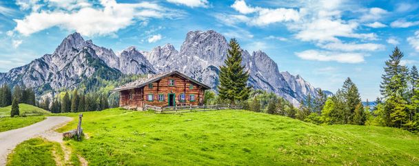 Panorámás kilátás festői hegyvidéki táj az Alpokban a hagyományos hegyi faház és a friss zöld rétek tavasszal - Fotó, kép