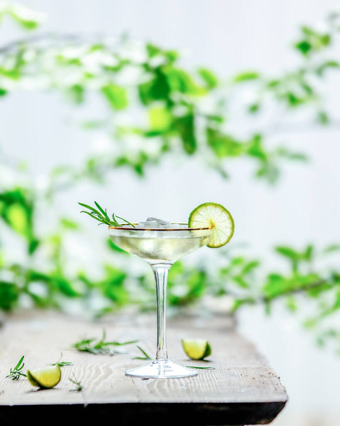 алкогольний коктейль з лаймом на столі і фоні з зеленими гілками
 - Фото, зображення