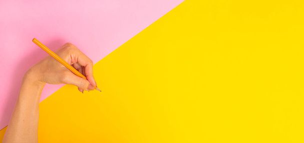 The left hand is holding a pencil and is about to write something on a bright pink-yellow background banner. International Left-handers Day on August 13 - Fotografie, Obrázek