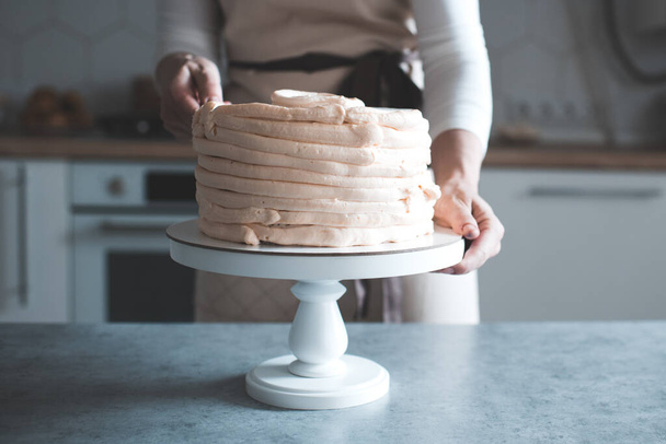Mujer decorando sabroso pastel con crema batida en bandeja de pie en primer plano de la cocina. Día de la boda. Fiesta de cumpleaños
.  - Foto, imagen
