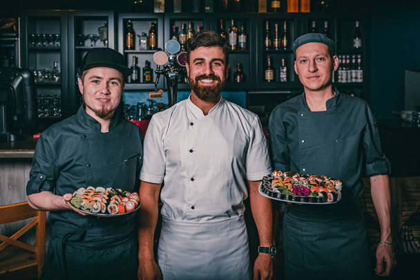 Portrait of three chefs in cafe showing plate with sushi - Photo, Image