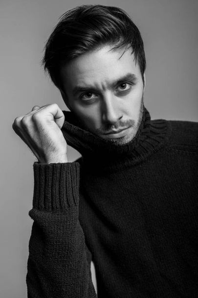 Portrait of sexy handsome man with stylish hairdo wearing warm sweater, pulling sweater collar and looking seductive, flirting at camera, male fashion, vogue concept. black and white, indoor isolated - Valokuva, kuva