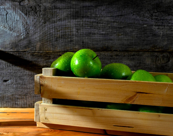 primo piano di molte mele fresche verdi con goccioline d'acqua in una cassa di legno. orario serale presso il magazzino frutta - Foto, immagini