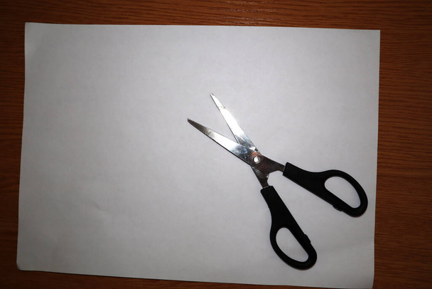 Černé nůžky na bílý kus papíru na stole - Fotografie, Obrázek
