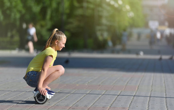 Girl child rides while sitting on a hoverboard in a summer park, happy and cheerful - Foto, Imagem