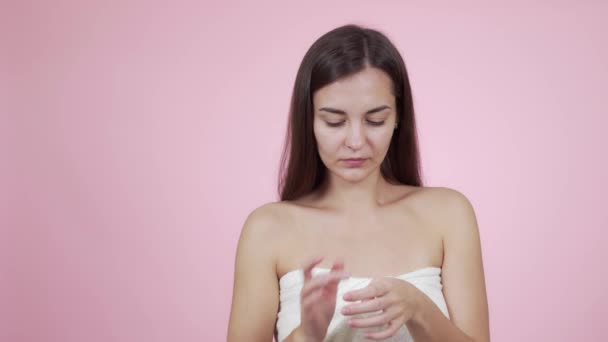 Portrait of beautiful woman applying face cream isolated on pink background - Záběry, video