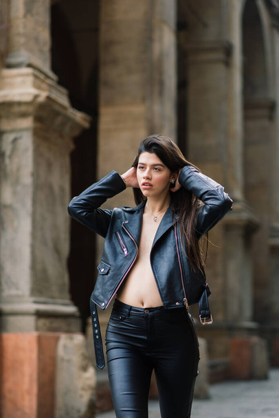 Ritratto di bella giovane donna bruna con elegante giacca di pelle nera, sorride su sfondo urbano, tempo felice, Travel Concept. - Foto, immagini
