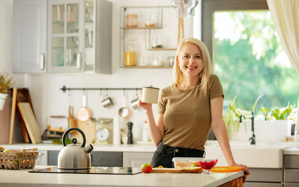 blondynka stoi w kuchni z filiżanką kawy - Zdjęcie, obraz
