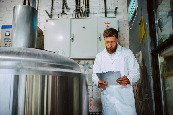 Caucasian male professional  technologist expert in white suit  operating production machine in food factory and doing quality control and holding checklist. Checking production in food industry. - Photo, Image
