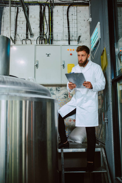 Blanke mannelijke professionele technoloog expert in witte pak het bedienen van de productiemachine in voedselfabriek en het doen van kwaliteitscontrole en het houden van checklist. Controle van de productie in de levensmiddelenindustrie. - Foto, afbeelding