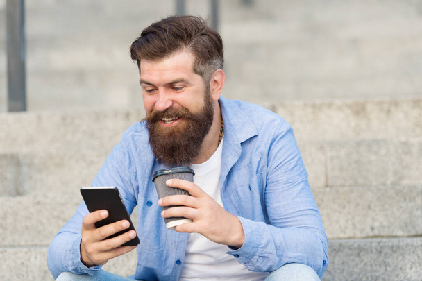 Modern life online communication. Guy with smartphone urban space background. Handsome bearded man relaxing mobile phone and coffee cup. Modern technology. Living online life. Social networks - Foto, Bild