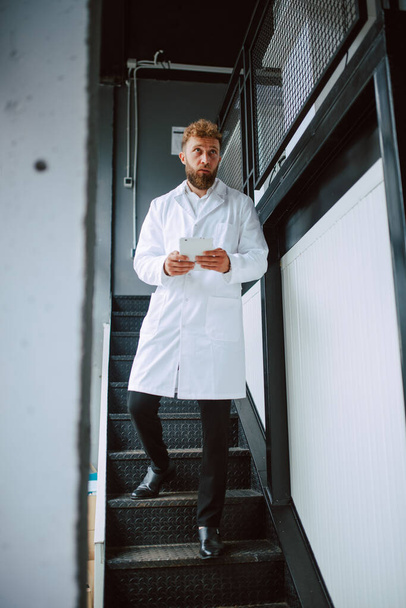 Profesionální kavkazský odborník na bílé uniformy stojí na stupních ve výrobním závodě - továrně  - Fotografie, Obrázek