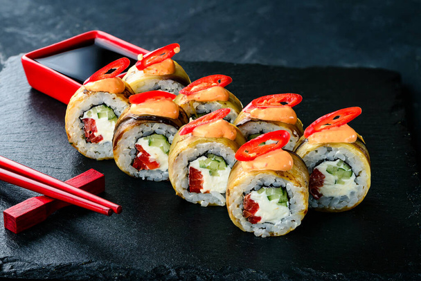 Traditional Japanese cuisine. Selective focus on set of sushi rolls with cream cheese, rice, chili pepper on dark background, spicy sushi with eggplant and chili pepper - Photo, image