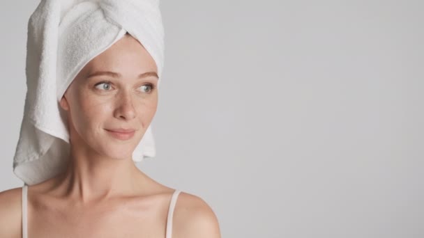 Gorgeous woman with towel on head happily looking aside on copy space and in camera over gray background - Footage, Video