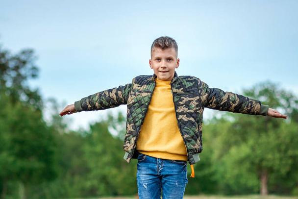 Un ragazzo corre attraverso il campo con le braccia tese su uno sfondo di verde. Il concetto di sogni, scelta della professione, pilota, infanzia. Copia spazio - Foto, immagini
