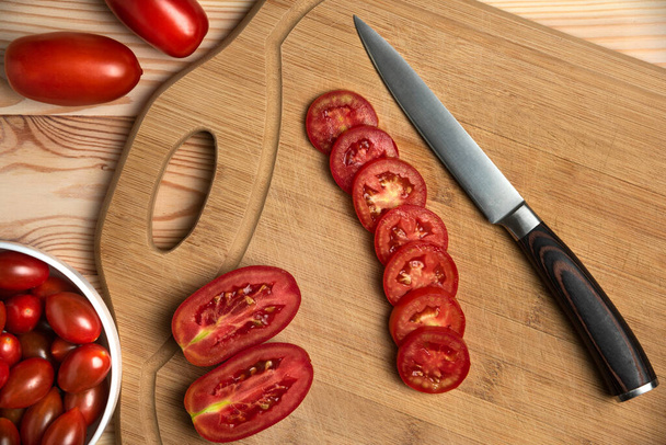 Red berries and sliced tomatoes on the wooden table - Photo, image