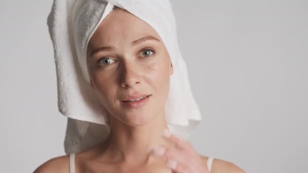 Młoda piękna kobieta z ręcznikiem na głowie dotknąć jej oczyszczone twarz zmysłowo patrząc w aparacie odizolowany - Materiał filmowy, wideo