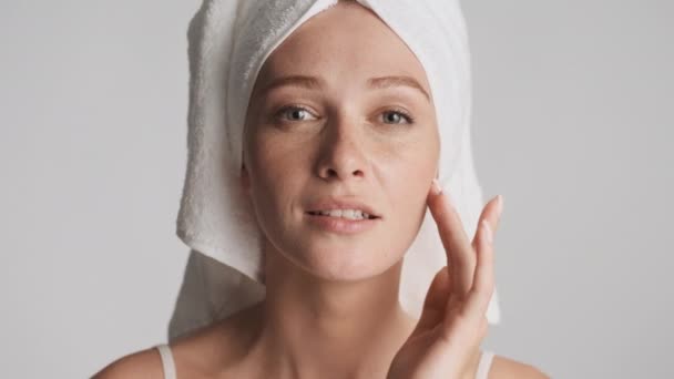 Νεαρή ελκυστική γυναίκα με πετσέτα στο κεφάλι αγγίξει καθαρό φρέσκο πρόσωπό της αισθησιακά κοιτάζοντας στην κάμερα απομονωμένη - Πλάνα, βίντεο