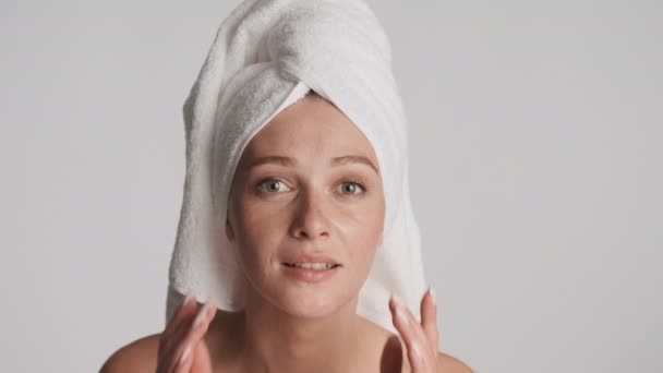 Close up bella donna con asciugamano sulla testa toccare il suo viso pulito sulla macchina fotografica su sfondo grigio - Filmati, video