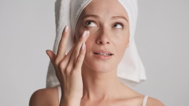 Portrait of attractive woman with towel on head happily applying moisturizing cream on face isolated - Footage, Video