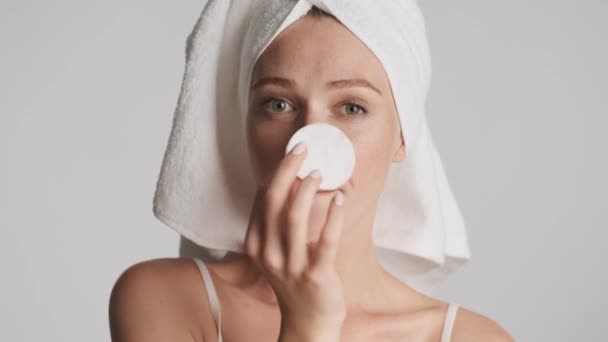 Pretty cheerful girl with towel on head and cotton sponge in hand joyfully posing on camera isolated. Fooling around expression - Footage, Video