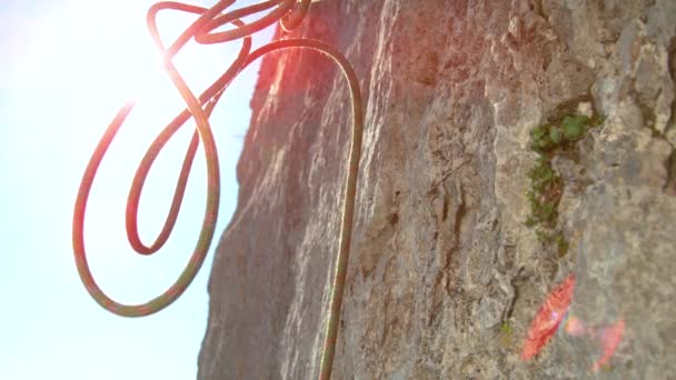 CLOSE UP, LENS FLARE: La cuerda verde y roja cae desde la cima de un imponente acantilado. - Metraje, vídeo