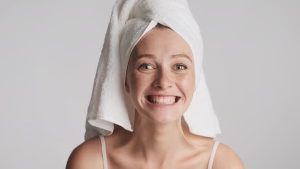 Jeune femme drôle attrayante avec une serviette sur la tête tenant la brosse à dents posant joyeusement montrant propre de ses dents sur fond gris. Se moquer de l'expression - Séquence, vidéo