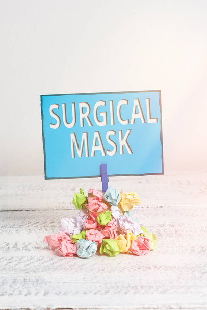 Πινακίδα κειμένου που δείχνει χειρουργική μάσκα. Εννοιολογική φωτογραφία φοριέται από επαγγελματίες υγείας κατά τη διάρκεια της χειρουργικής επέμβασης και κατά τη διάρκεια της νοσηλευτικής Υπενθύμιση σωρό χρωματισμένο τσαλακωμένο χαρτί clothespin υπενθύμιση λευκό ξύλινο χώρο. - Φωτογραφία, εικόνα