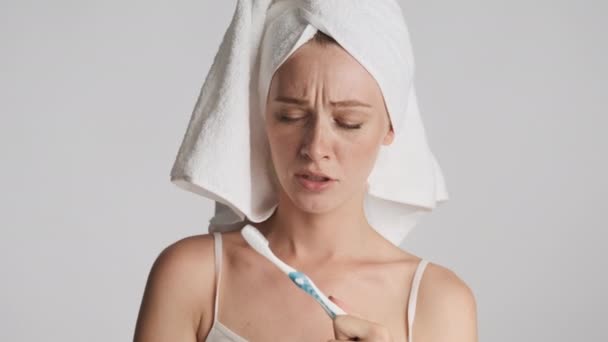 Jovem mulher atraente olhando atentamente escova de dentes mostrando limpo de seus dentes e acenando sem gesto na câmera sobre fundo cinza. Não o aconselha
 - Filmagem, Vídeo